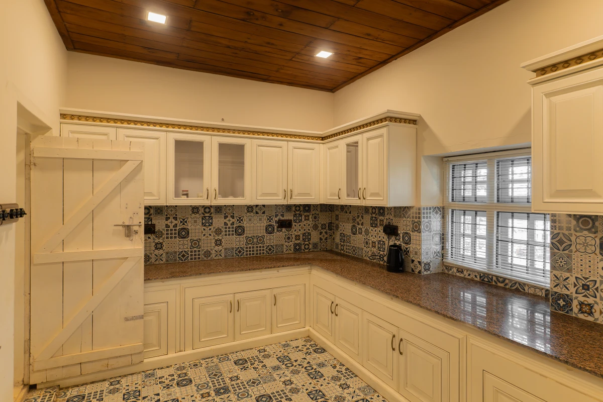 Fully Equipped Kitchen with Classic Cabinets Fully equipped kitchen with classic white cabinets and patterned tiles at boCHE 1000 Acre, one of the best resorts in Wayanad.